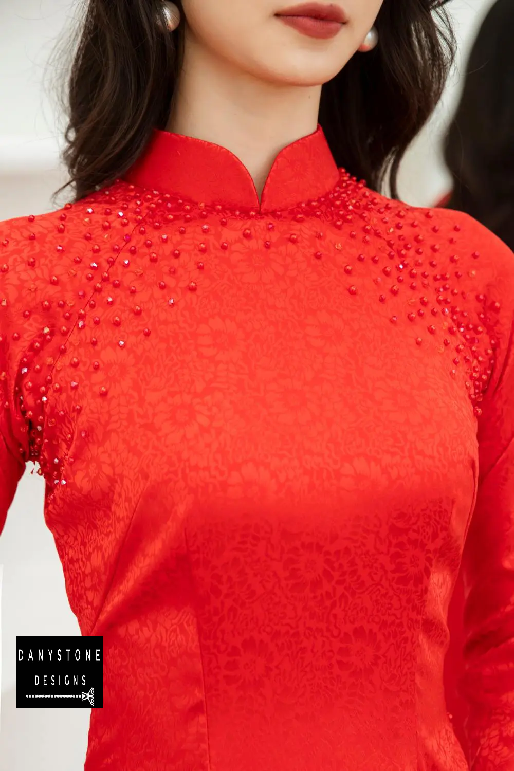 Close-up of the intricate pattern and red pearl beads on the Red Brocade Ao Dai, highlighting meticulous craftsmanship.