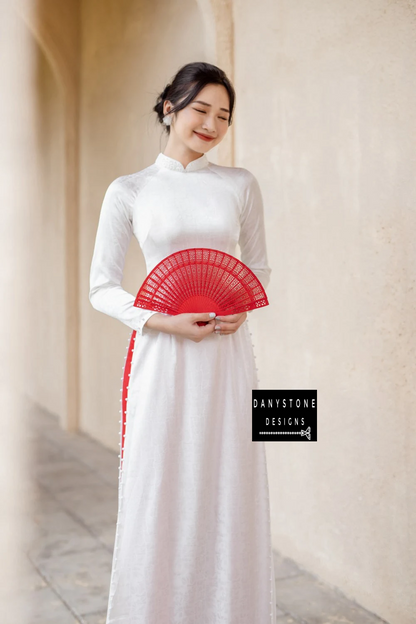 Bride holding a red fan in the White Brocade Ao Dai, illustrating the elegant and sophisticated beauty of the dress.