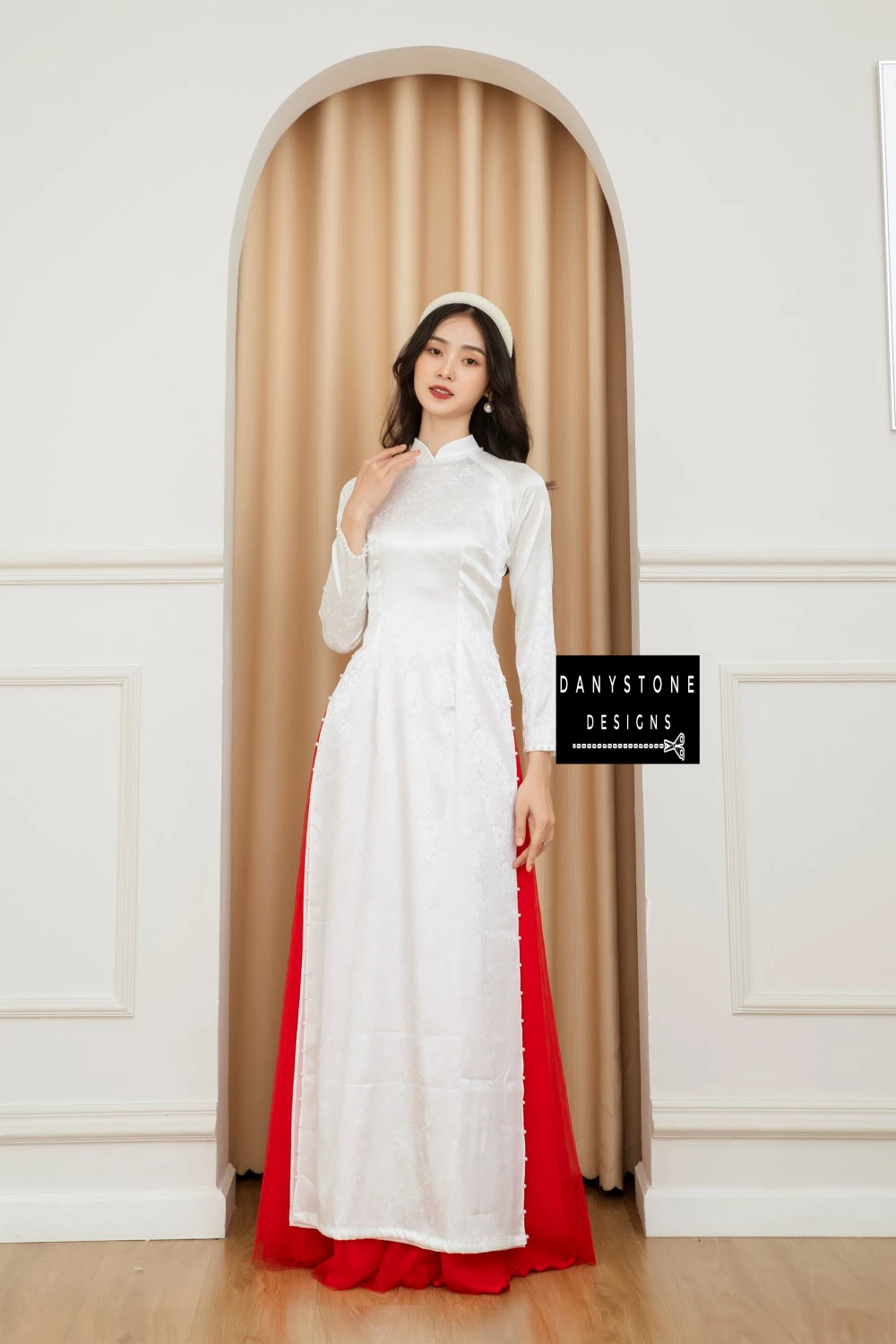 Full-length view of a bride wearing the Pure White Brocade Ao Dai with jade border, standing gracefully in an arched doorway.