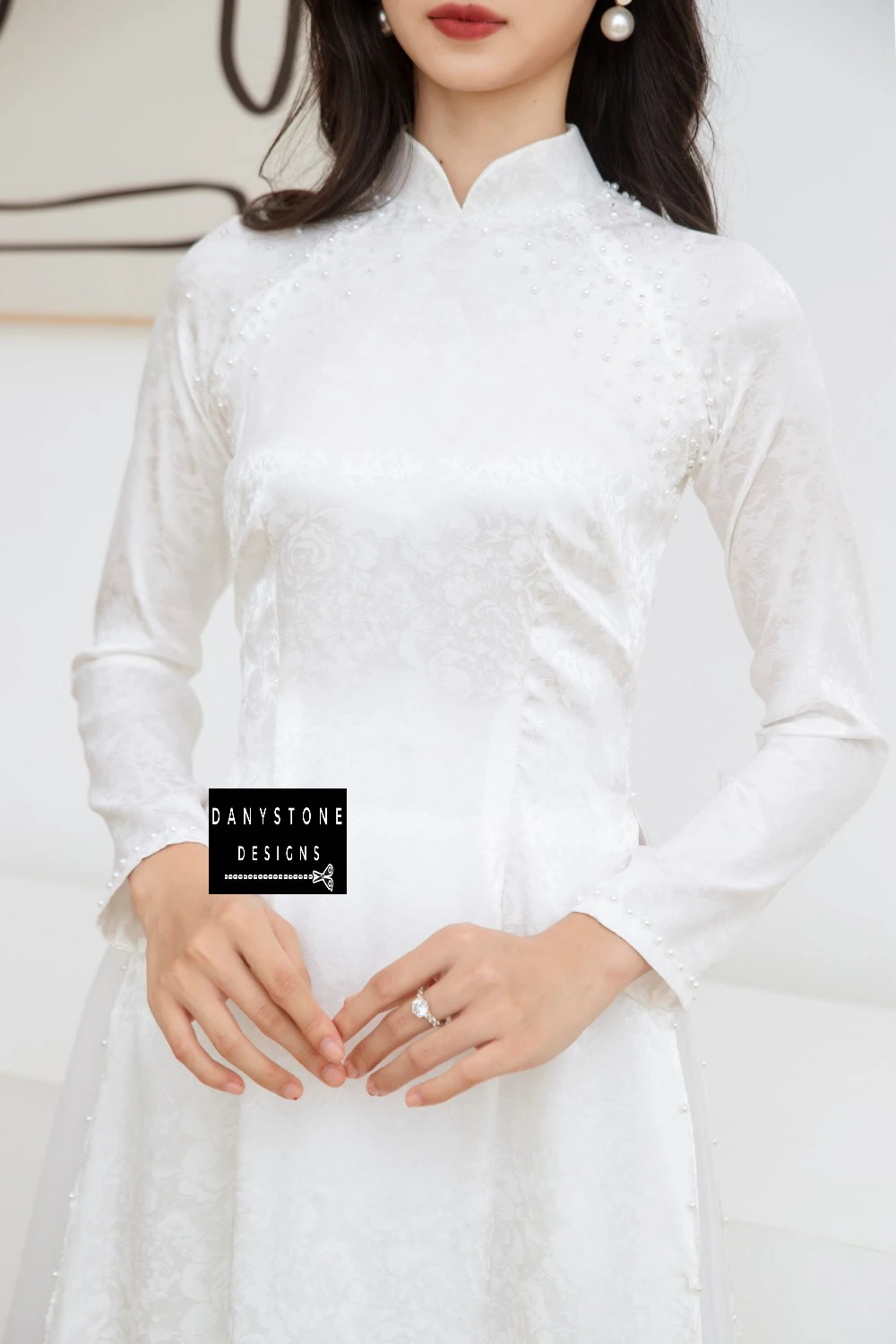 Detail shot of the pearl-studded neckline and intricate brocade patterns on the Elegant White Brocade Bridal Ao Dai.