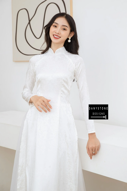 Full-length view of a bride wearing the Elegant White Brocade Bridal Ao Dai, standing elegantly in a modern setting.