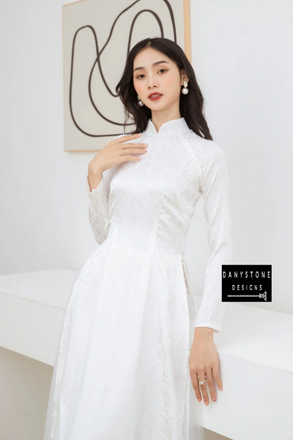 Side profile of a bride in the Elegant White Brocade Bridal Ao Dai, highlighting the soft brocade fabric and pearl details on the sleeves.