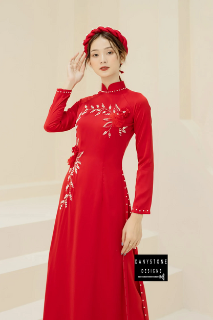 Luxurious red silk Áo Dài with elegant jade flower and pearl branch details, worn by a bride.