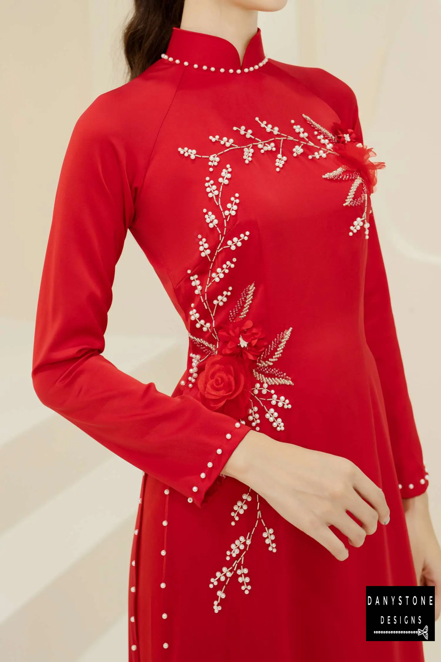 Elegant woman wearing a red silk bridal Áo Dài with jade flowers and pearl branch details.