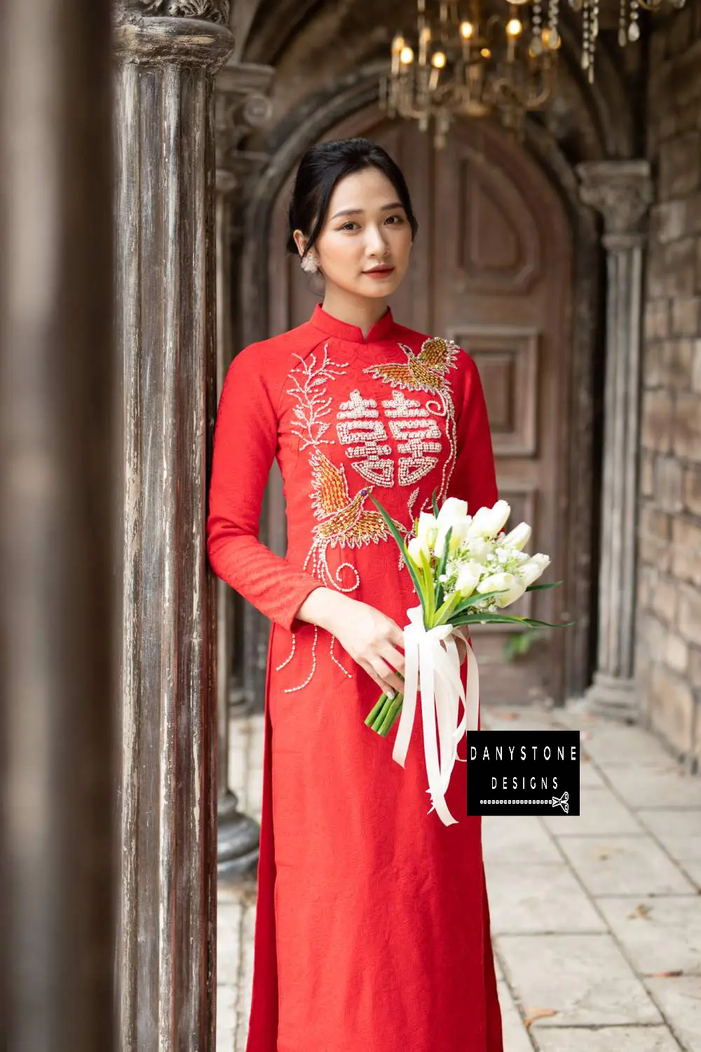 Full-length view of a bride in a red brocade Áo Dài with intricate phoenix details. 