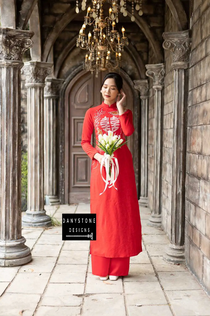 Red brocade Áo Dài with elegant phoenix embroidery and a beaded joy symbol, worn by a bride.