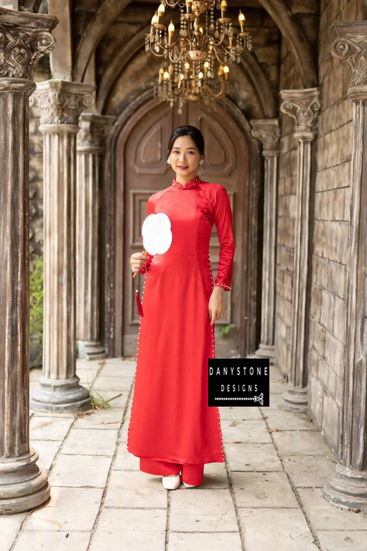  Elegant woman wearing a red brocade Áo Dài with beaded collar and pearl details.