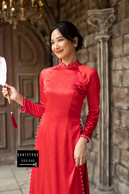 Woman in a red brocade Áo Dài, featuring intricate embroidery and beaded details.