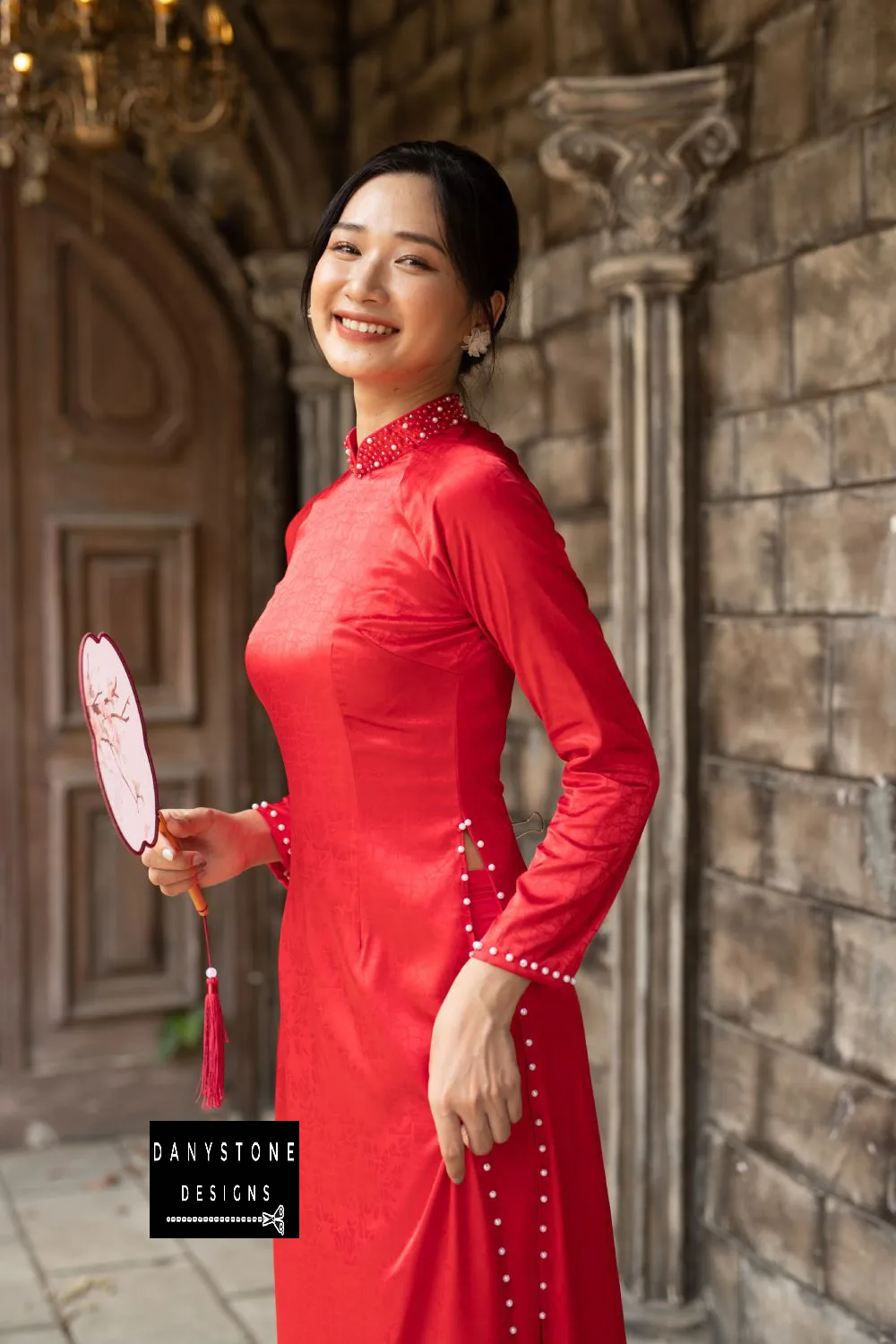 Side view of a red brocade Áo Dài with pearl-decorated sleeves and hem.