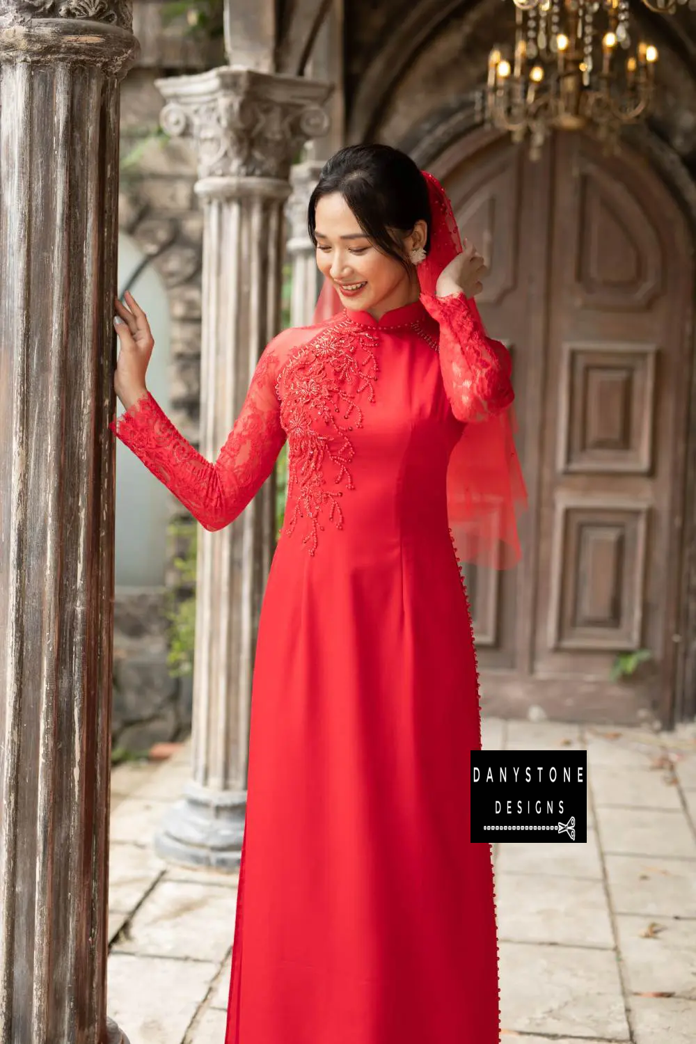 Full-length view of a bride in a red silk Áo Dài with intricate beaded flowers and leaves.