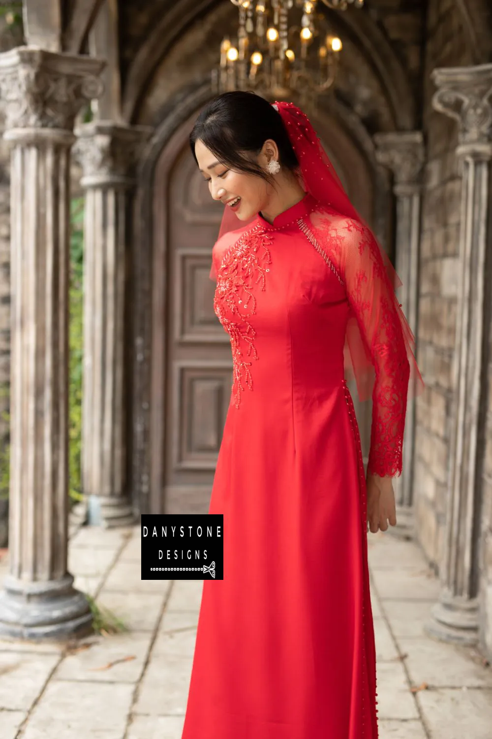 Woman in a red silk Áo Dài, featuring see-through lace sleeves and beaded embellishments.