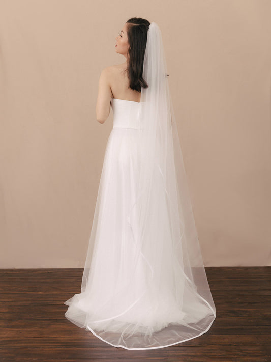 Woman wearing a strapless wedding dress with a long veil against a beige background