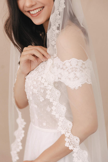 Woman wearing a white lace wedding dress with a veil against a beige background