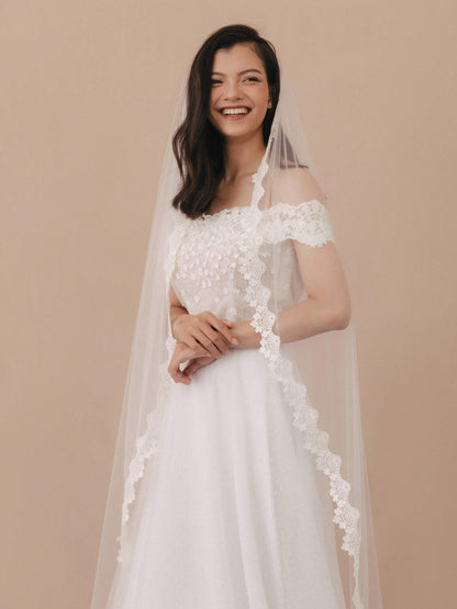 Woman wearing a white wedding dress with floral lace details on a beige background