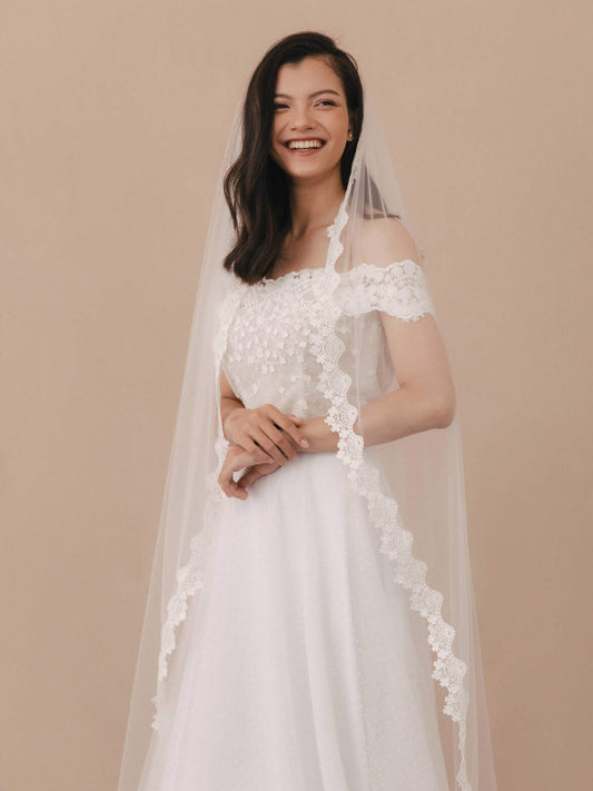 Woman wearing a white wedding dress with floral lace details on a beige background