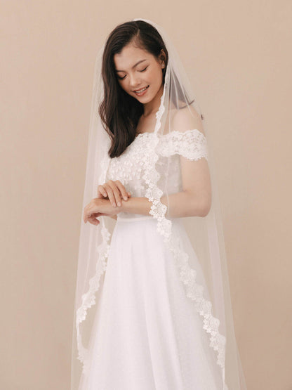 Woman wearing a white wedding dress with a lace veil against a beige background