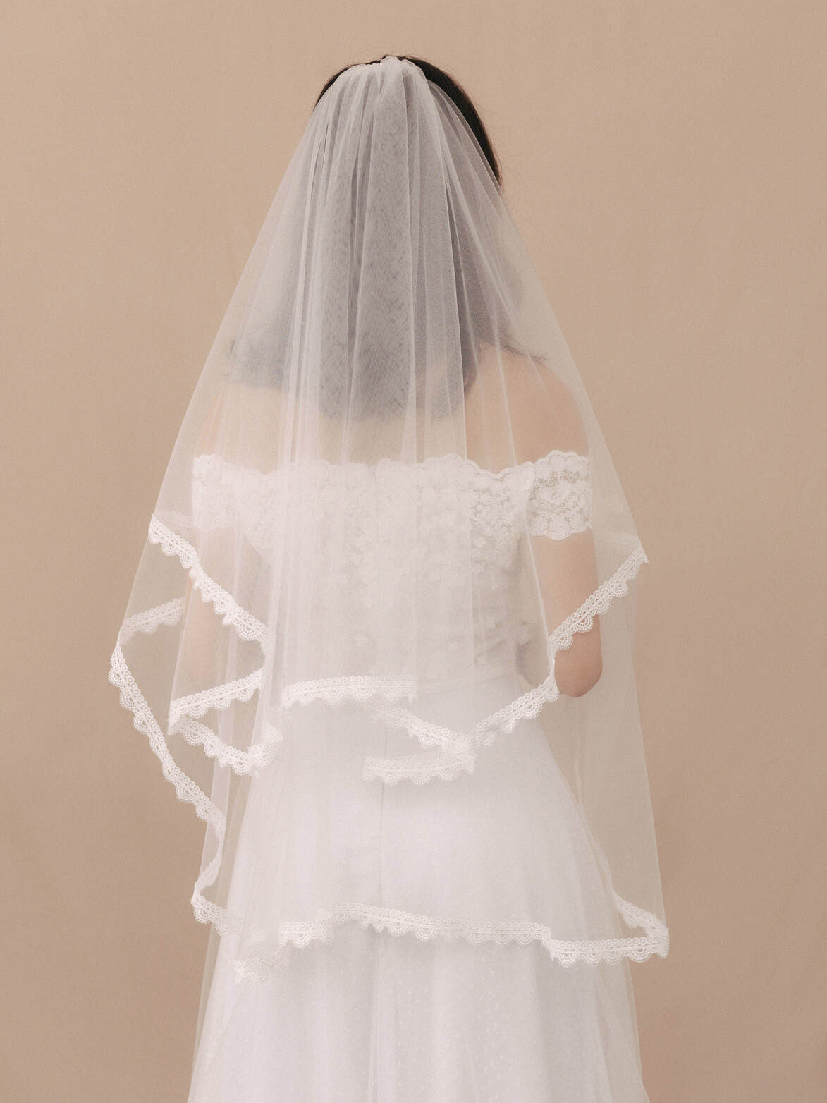 Bride wearing a white wedding dress with a veil against a beige background