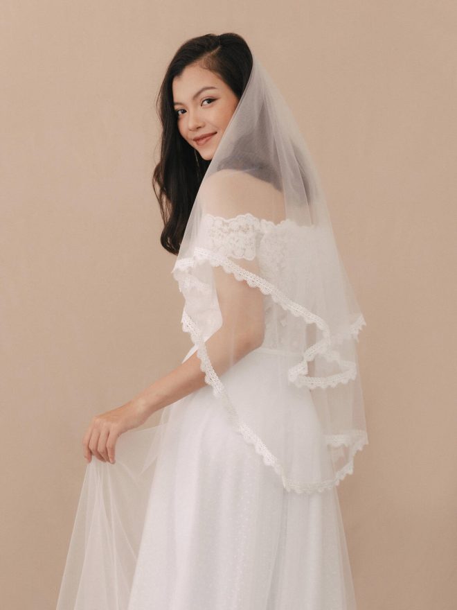 Woman wearing a white lace veil against a beige background