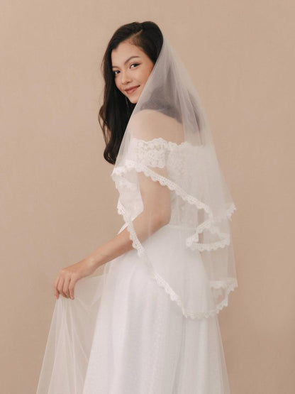Woman wearing a white lace veil against a beige background