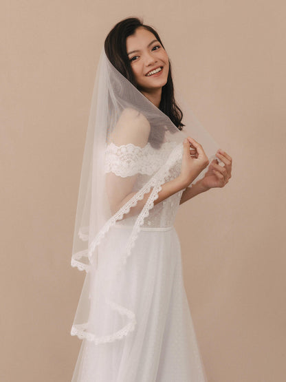 Woman wearing a white lace wedding dress with a matching veil against a beige background