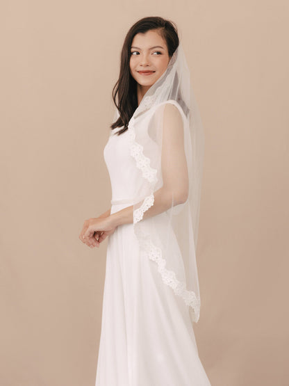 Woman wearing a white wedding dress with a sheer overlay against a beige background