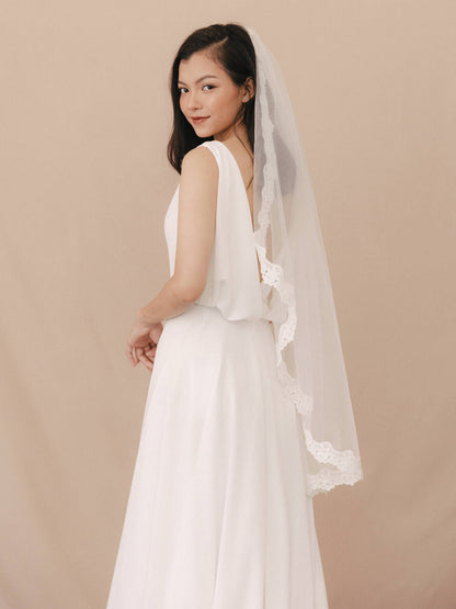 Woman wearing a white wedding dress with a veil against a beige background