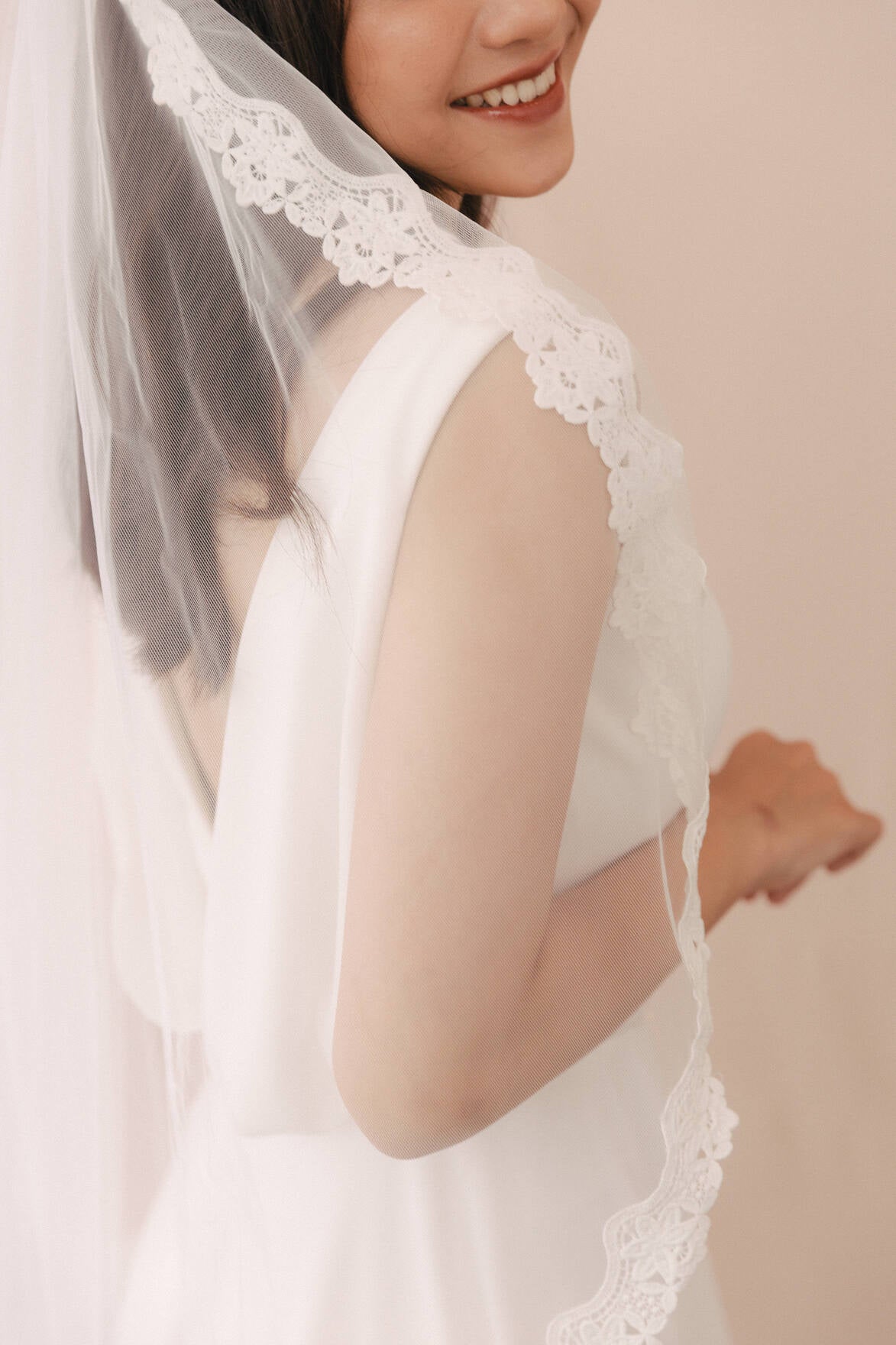 Woman wearing a white lace veil against a neutral background