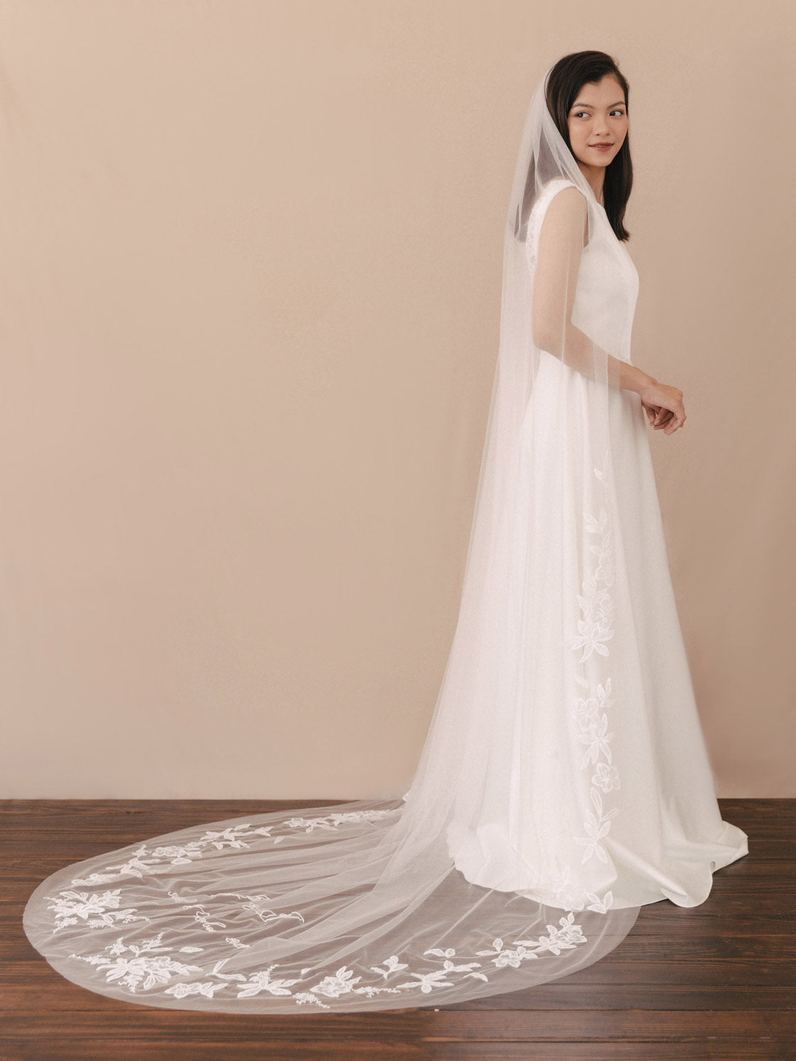 Woman wearing a white wedding dress with a long veil on a plain background