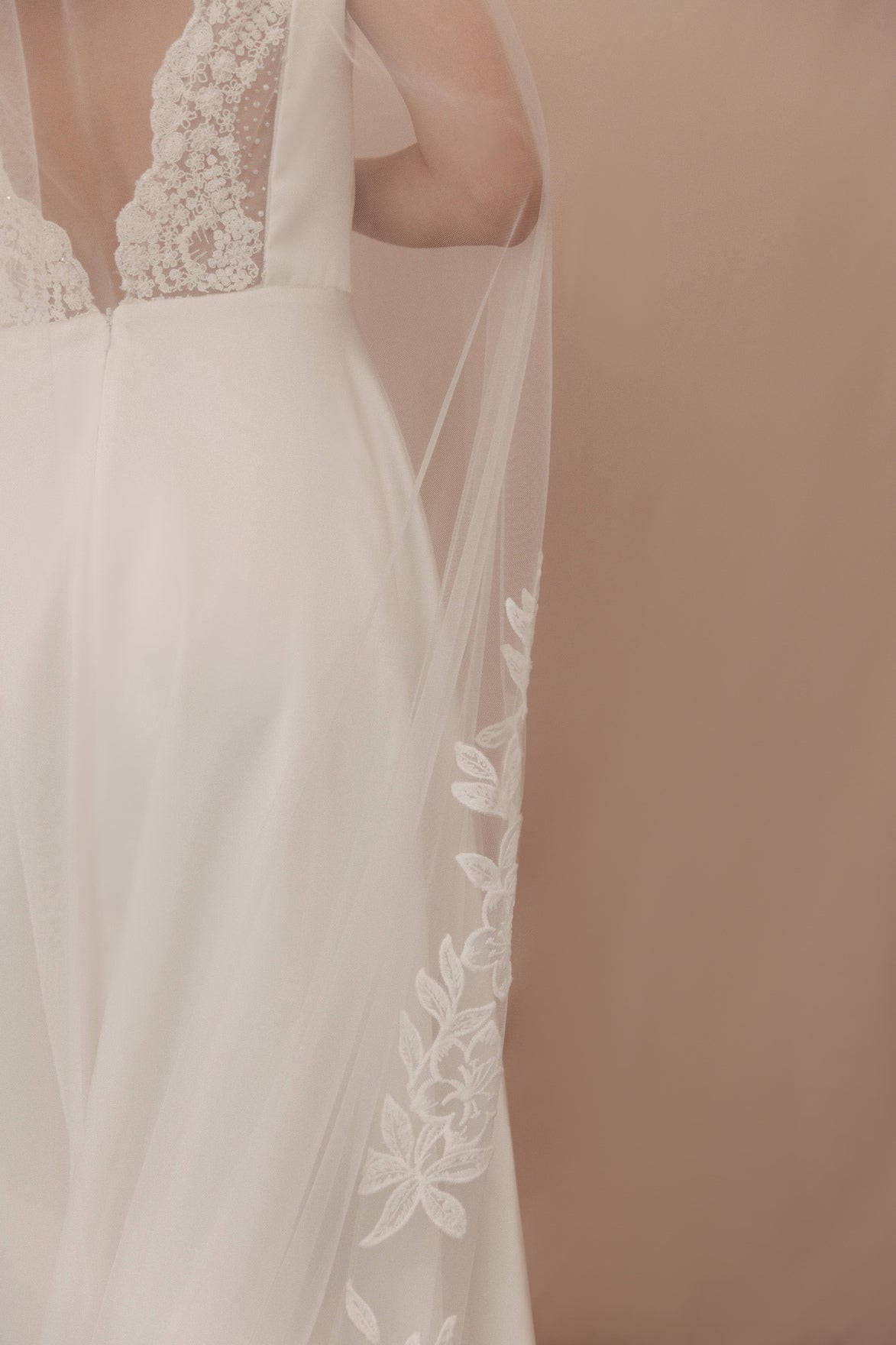 Close-up of a wedding dress with lace detailing on a plain background