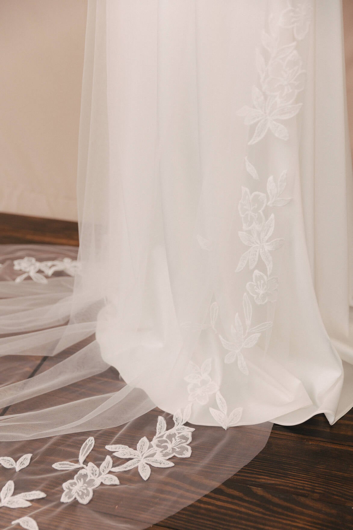 White wedding dress with floral lace details on a wooden floor.