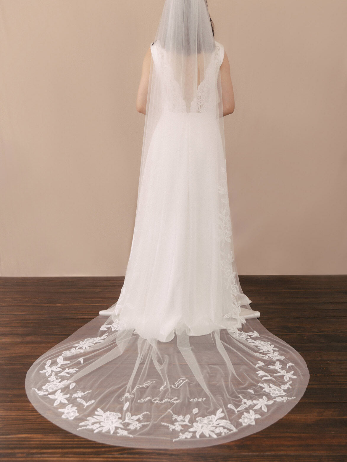 White wedding dress with a long train and lace details on a wooden floor.