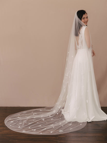 Woman wearing a white wedding dress with a long veil against a beige wall.