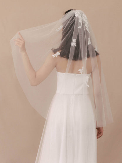 Woman wearing a white wedding dress with a floral veil against a beige background