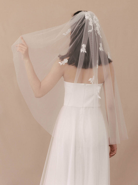 Woman wearing a white wedding dress with a floral veil against a beige background