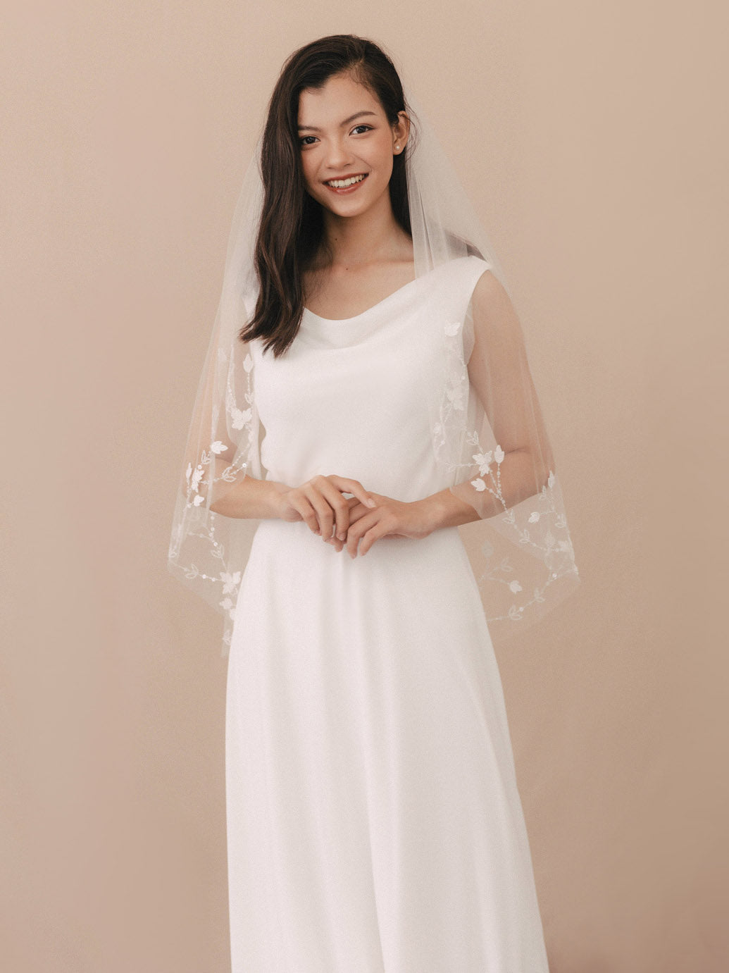 Woman wearing a white wedding dress with a sheer overlay on a beige background