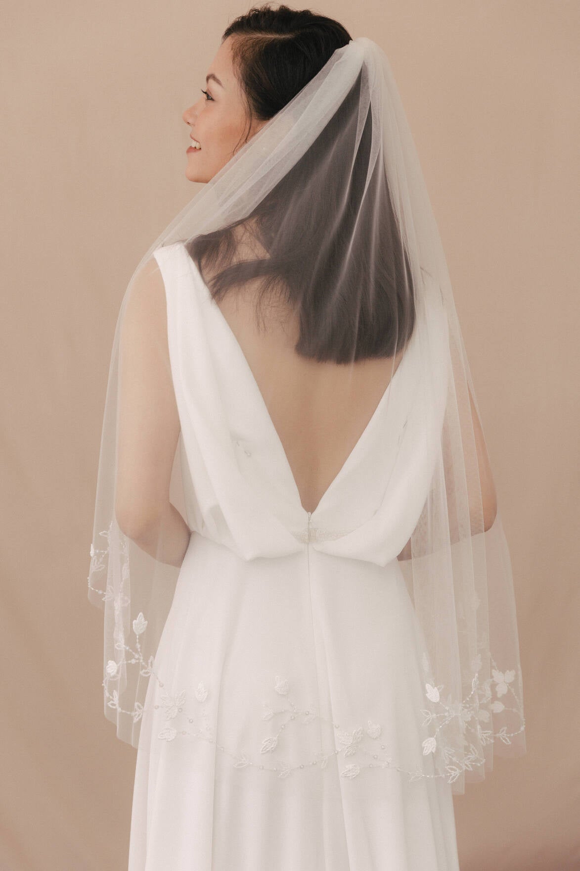 Woman wearing a white wedding dress with a sheer veil against a beige background