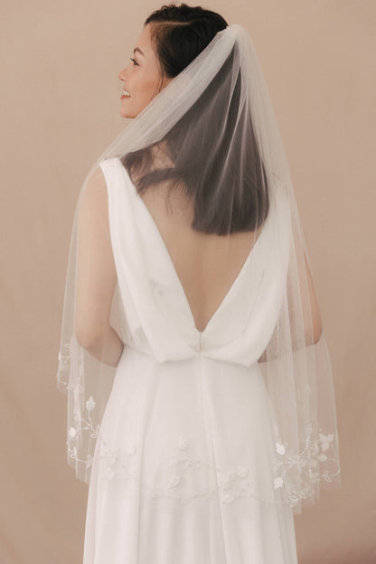 Woman wearing a white wedding dress with a sheer veil against a beige background