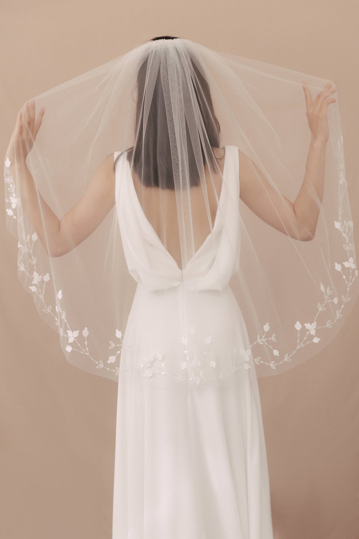 Woman wearing a white wedding dress with a veil against a beige background