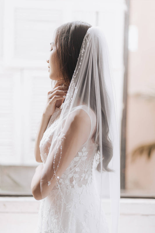 Woman wearing a white wedding dress with a veil in a softly lit room.