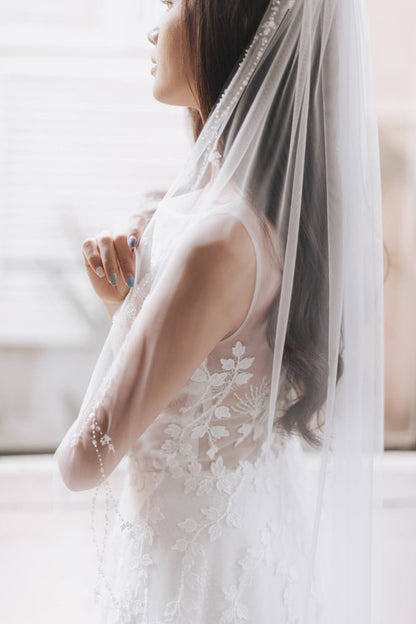 Woman wearing a white lace wedding dress with a veil indoors.