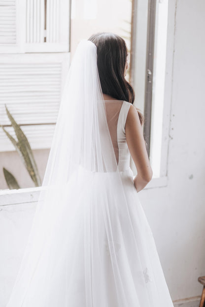 Woman in a white wedding dress with a long veil standing in a bright room.