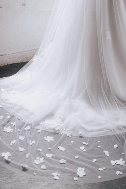 Close-up of a white wedding dress with floral details on a neutral background