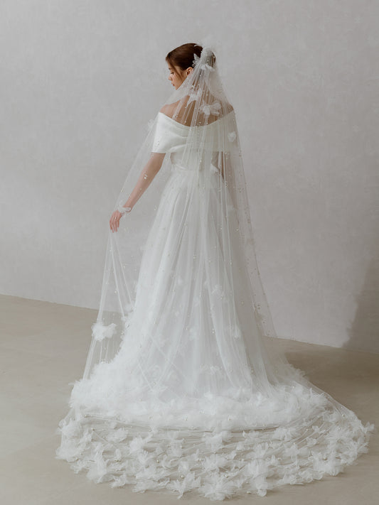 Woman wearing a white wedding dress with a long veil against a plain background