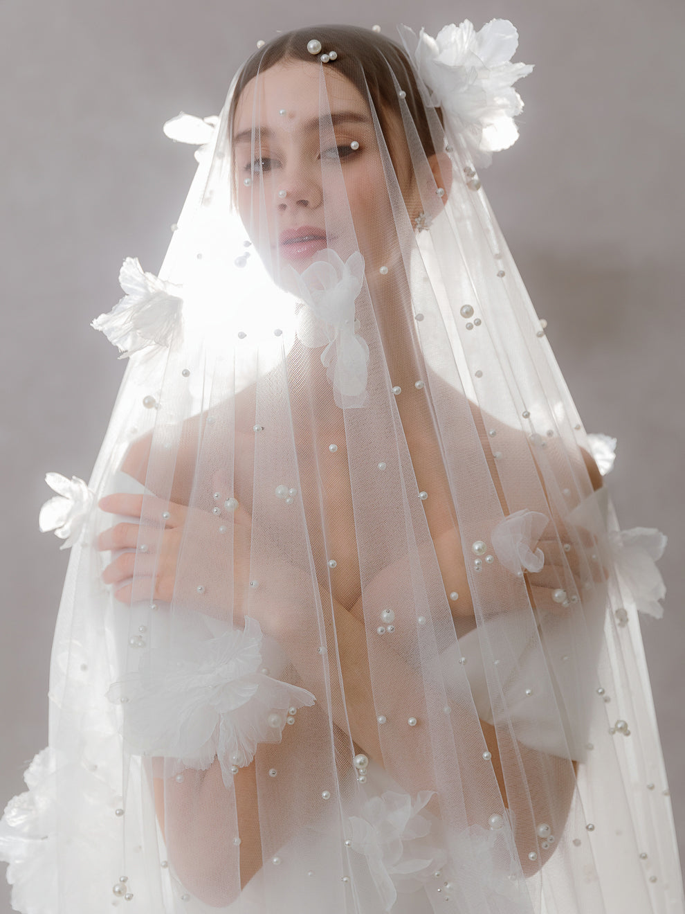 Woman wearing a delicate white veil with floral and pearl details on a neutral background