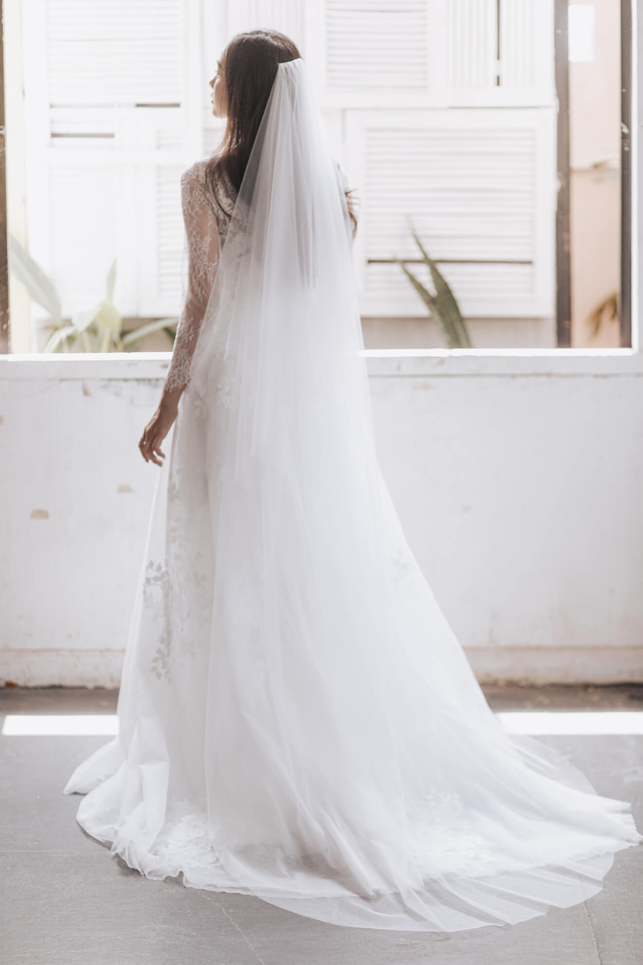 Woman wearing a white wedding dress with a long veil indoors.