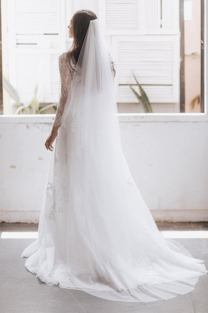 Woman wearing a white wedding dress with a long veil indoors.