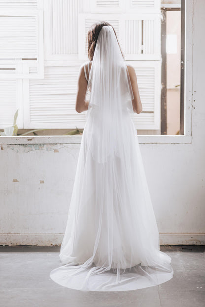 Woman wearing a long white wedding dress with a matching veil in a bright room.