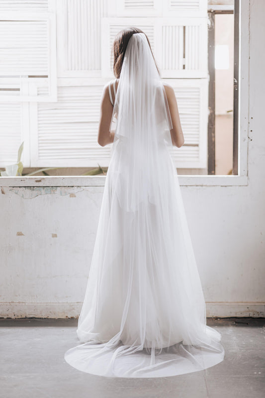 Woman wearing a long white wedding dress with a matching veil in a bright room.