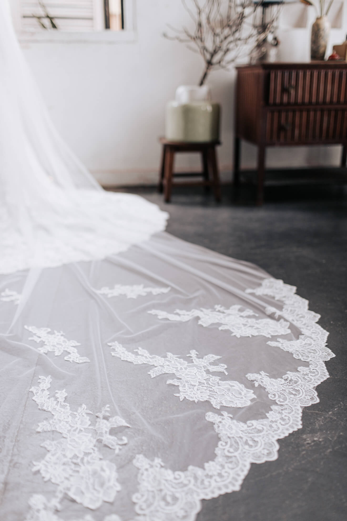 Close-up of a white lace wedding dress on a dark surface with a blurred indoor background.