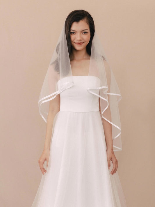 Woman wearing a white wedding dress with a veil against a beige background